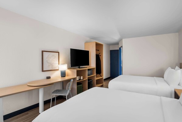 A hotel room with two beds, a desk with a chair, a television, a wardrobe, and a door.