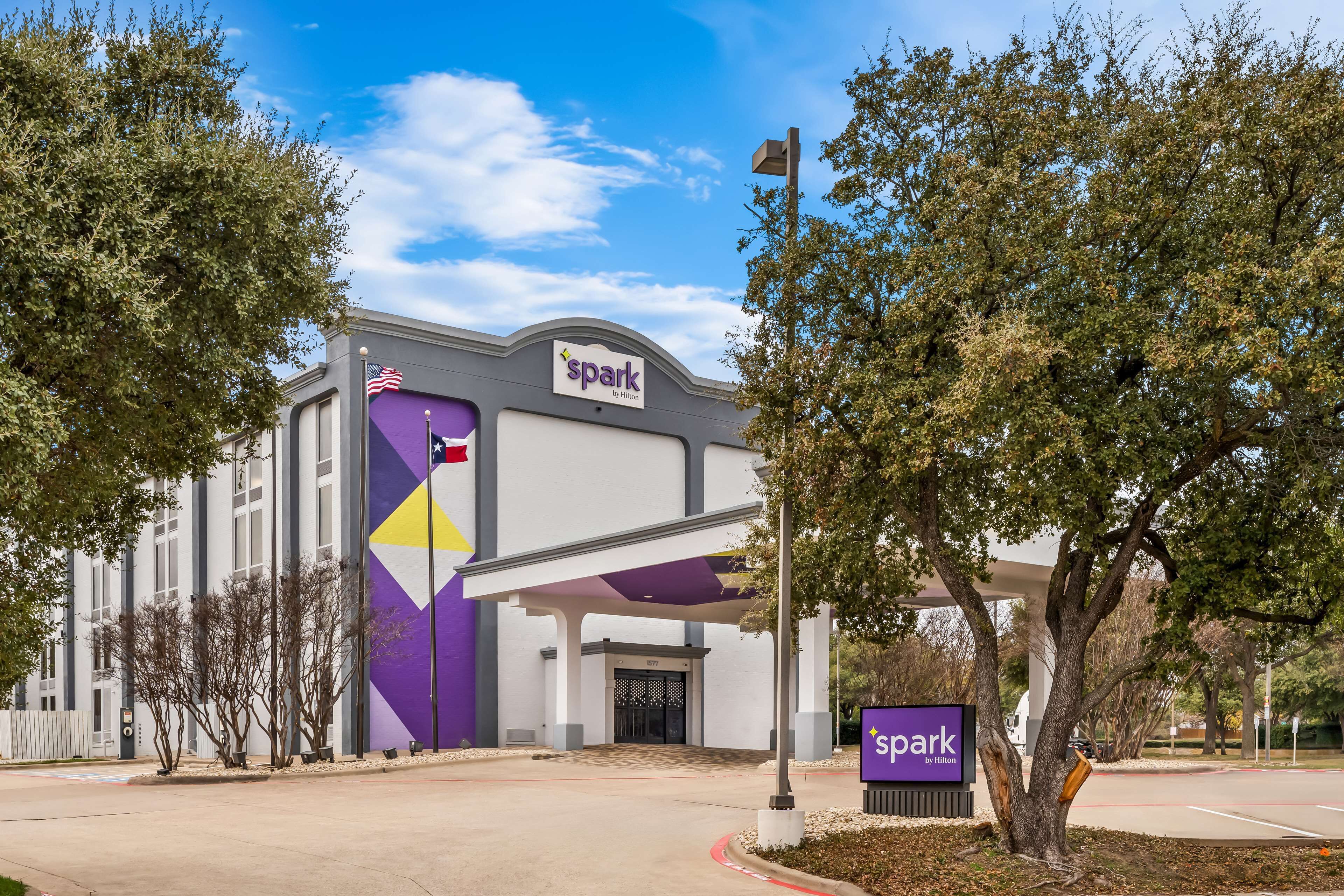 A hotel entrance with a purple and white facade, an American flag, and a sign reading "spark by Hilton".