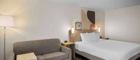 Una habitación de hotel con cama, sofá, mesita de noche y lámpara.