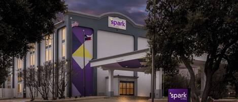 A hotel entrance with a 'spark by Hilton' sign, a covered entrance, and a flag.