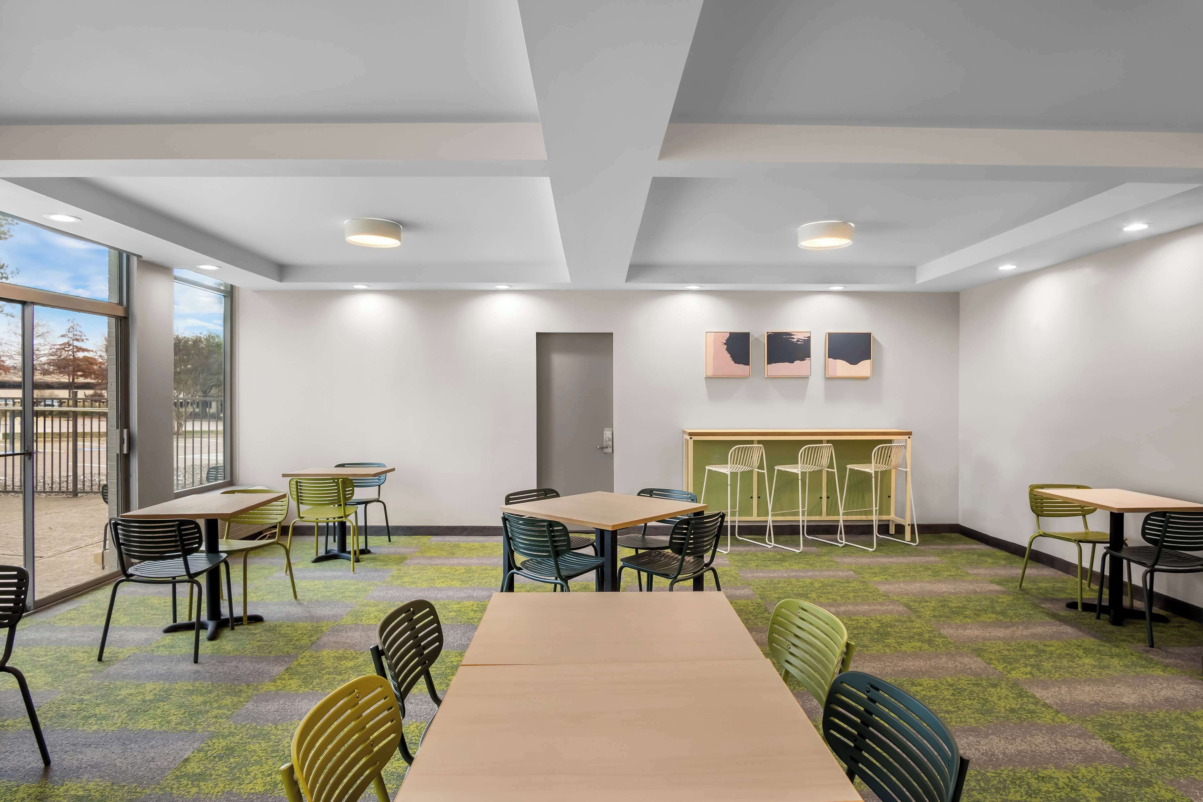 Une salle de conférence équipée de tables et de chaises, de grandes fenêtres et d’une porte.