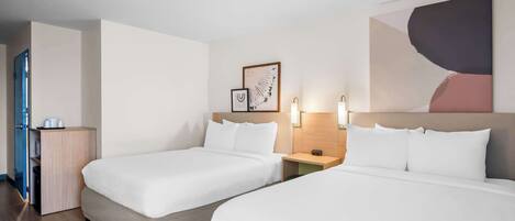 A hotel room with two beds, a wooden nightstand, a wall-mounted light, and a door to the left.
