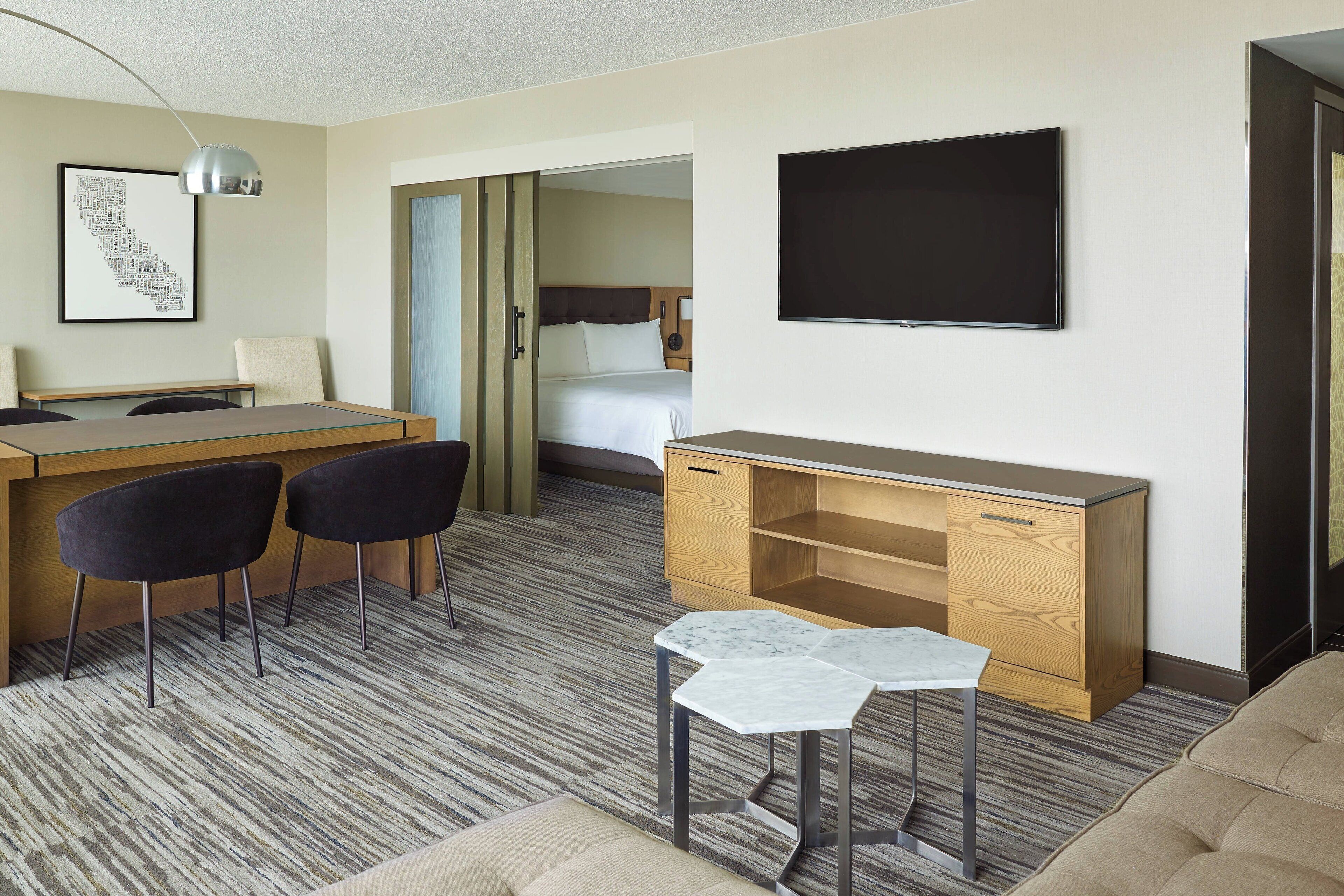 Ein Hotelzimmer mit einem Holztisch, zwei Stühlen, einem kleinen Tisch, einem Bett, einem Fernseher und einem gerahmten Bild an der Wand.