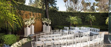 A garden setting with white chairs arranged in rows, a wooden fence, and a hedge in the background.