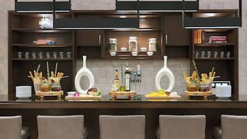 A bar area with a long counter, multiple shelves with glassware, and a variety of food and drink items displayed.