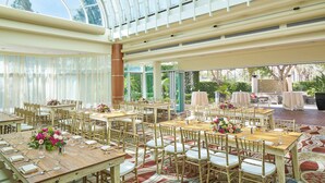 Un vaste espace intérieur aménagé pour les repas, avec de hauts plafonds et de grandes fenêtres, comprenant de nombreuses tables et chaises disposées pour accueillir les convives.