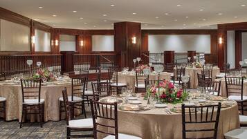 A banquet hall with round tables set for dining, featuring wooden chairs and white tablecloths.