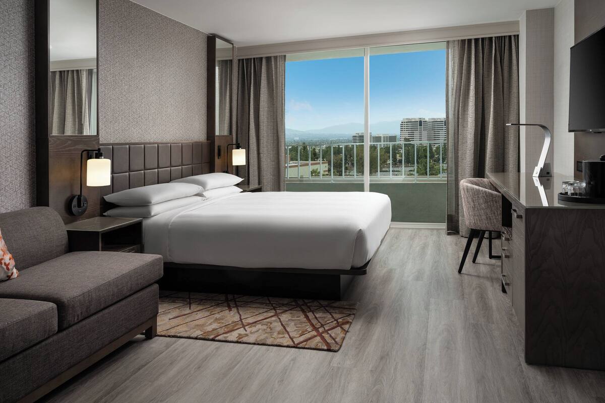 Una habitación de hotel moderna con una cama grande, un sofá, un escritorio y vistas a la ciudad.