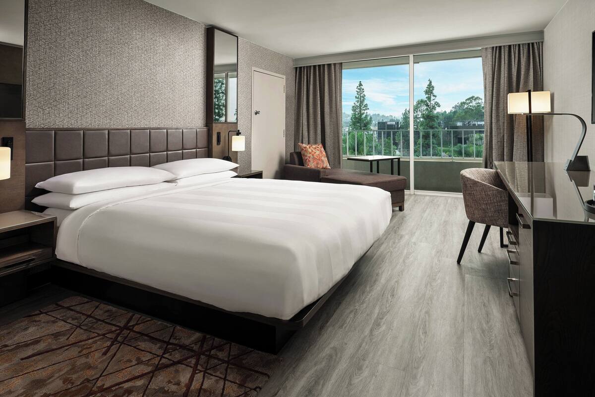 Habitación de hotel moderna con una cama grande, un escritorio y vistas al exterior.