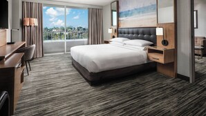 Une chambre d’hôtel avec un grand lit, un bureau, une chaise, une télévision et un balcon offrant une vue sur la ville.