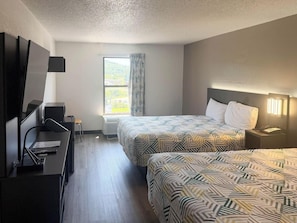 A hotel room with two beds, a desk, a chair, a television, and a window with curtains. - Econo Lodge near the Blue Ridge Parkway I-77 (Fancy Gap)