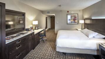 A hotel room with a bed, a desk with a chair, a dresser, a large mirror, and a framed picture on the wall.