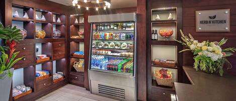 Restaurante Herb N' Kitchen con un mostrador refrigerado, estanterías de madera con varios artículos y un cartel que indica la ubicación.