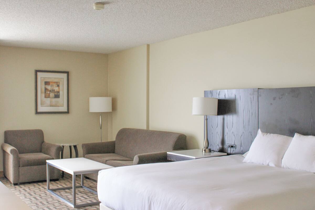 A hotel room with a bed, two armchairs, a small table, a TV, and a lamp.