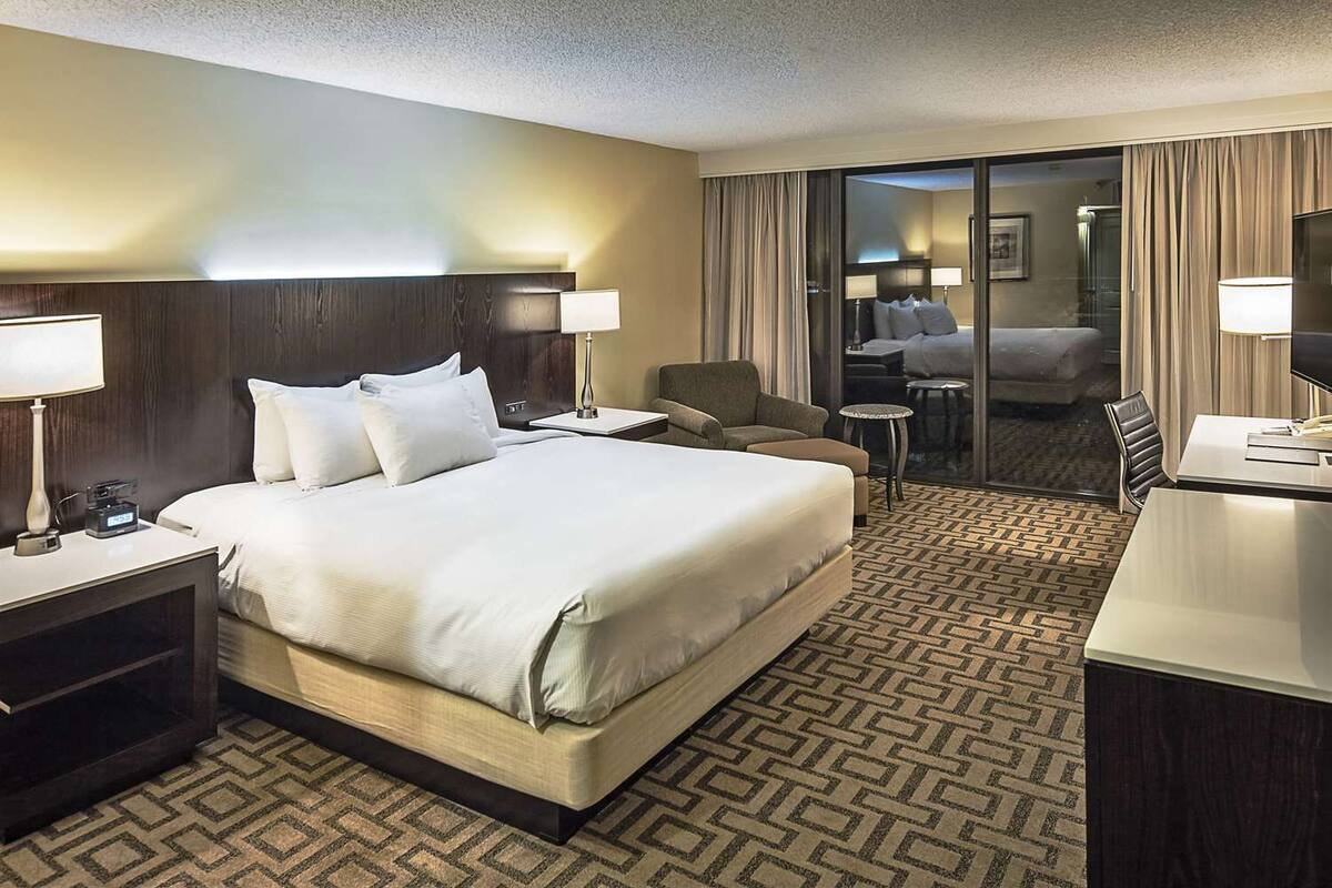 A hotel room with a large bed, a desk, a chair, a small table, and a view of a balcony with a sofa.