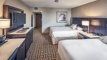A hotel room with a TV, two beds, a desk, and a patterned carpet.