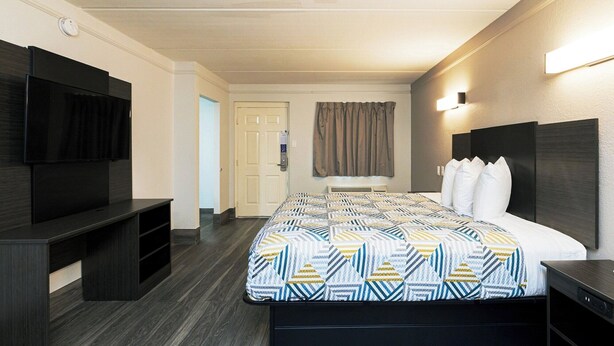 A hotel room with a bed, a TV, a desk, and a door. - Motel 6 Baytown, TX - Garth Rd (Baytown)