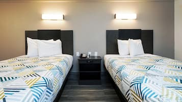 A hotel room with two beds, each with a patterned bedspread, a nightstand with a phone and a lamp, and wall-mounted lights.