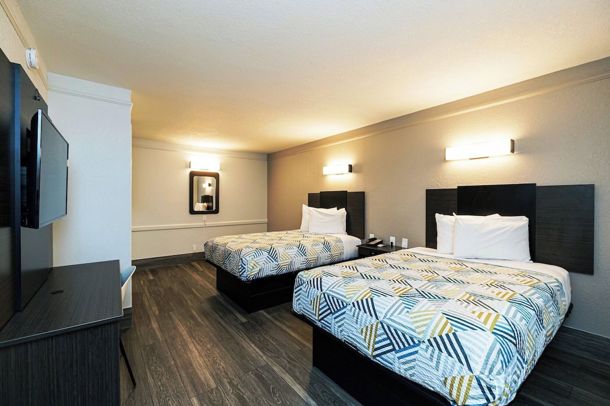A hotel room with two beds, a desk, a TV, and a mirror.