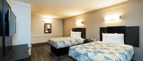 Quarto de hotel com duas camas, uma escrivaninha, televisão e espelho.
