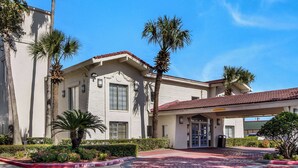 A building with a red-tiled roof, a covered entrance, and palm trees. - Motel 6 Baytown, TX - Garth Rd (Baytown)