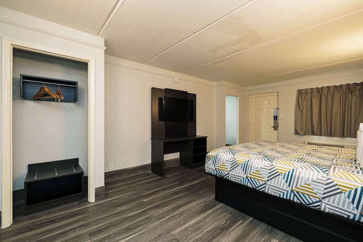 A bedroom with a bed, a TV, a coat rack, and a wardrobe.