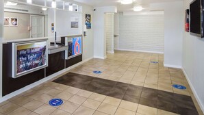 A reception area with a counter, a digital screen, and directional floor markers. - Motel 6 Baytown, TX - Garth Rd (Baytown)