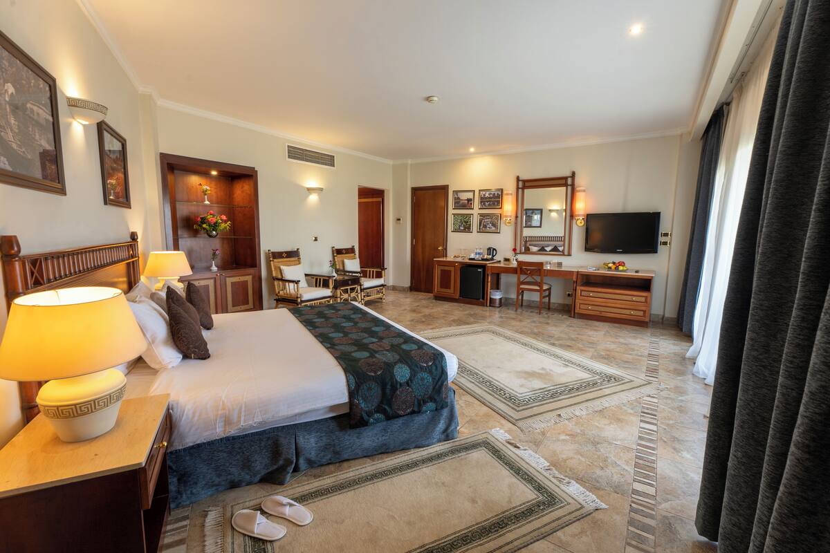 A hotel room with a large bed, a desk, a chair, a television, and a bathroom.