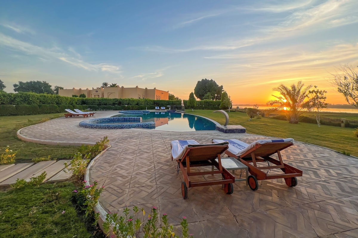 A swimming pool area with lounge chairs and a view of a sunset.