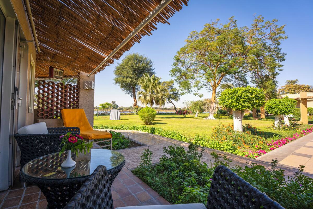 An outdoor seating area with wicker furniture, a glass table, and a thatched roof.