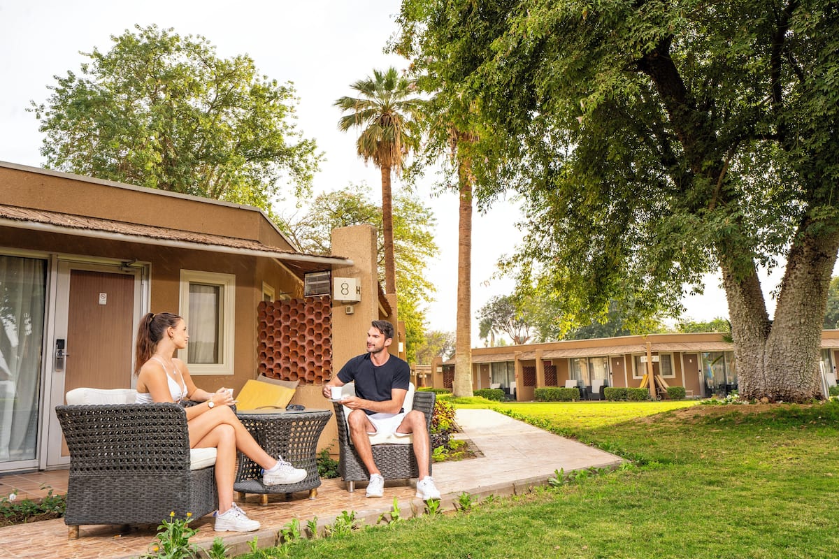 A couple sitting on wicker furniture outside a building with a palm tree and a well-maintained lawn.