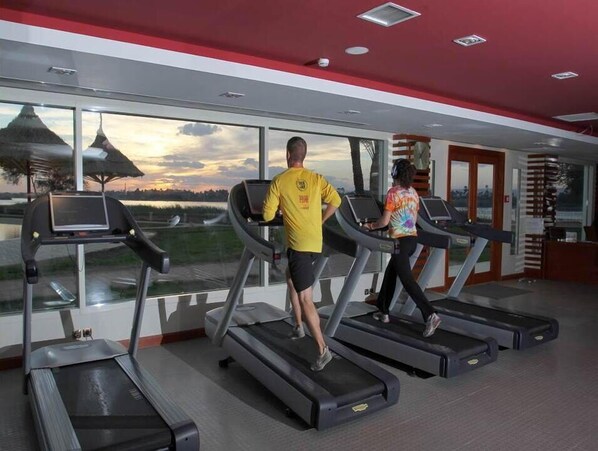 A gym with treadmills, large windows, and a view of a sunset over a landscape. - Jolie Ville Hotel & Spa Kings Island Luxor (Luxor)