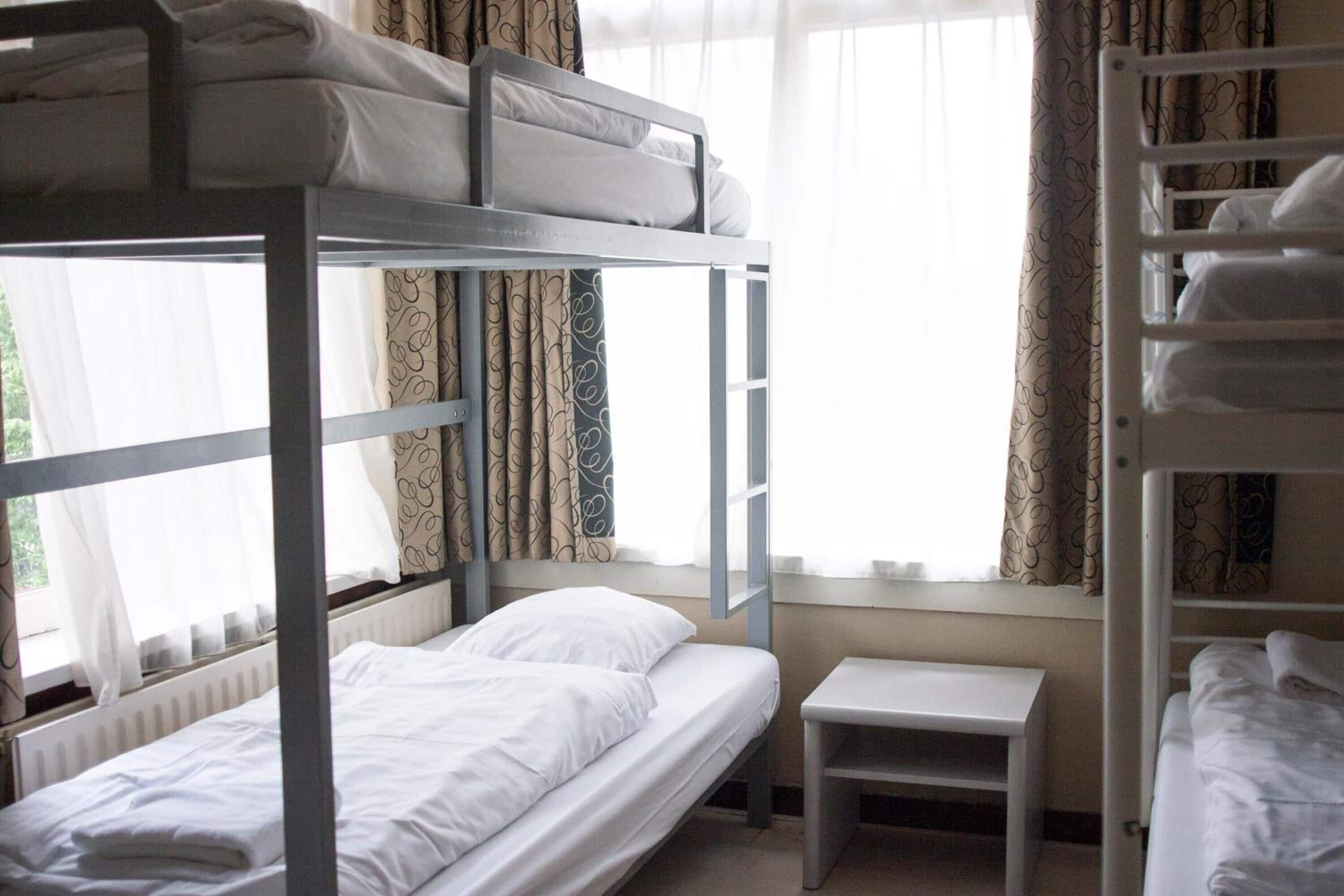 Une chambre avec un lit superposé, une petite table et une fenêtre avec des rideaux.