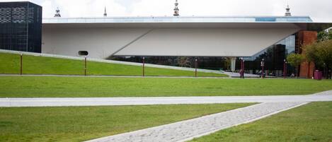 A modern building with a flat roof and a sloped side, surrounded by a grassy area and a paved walkway.