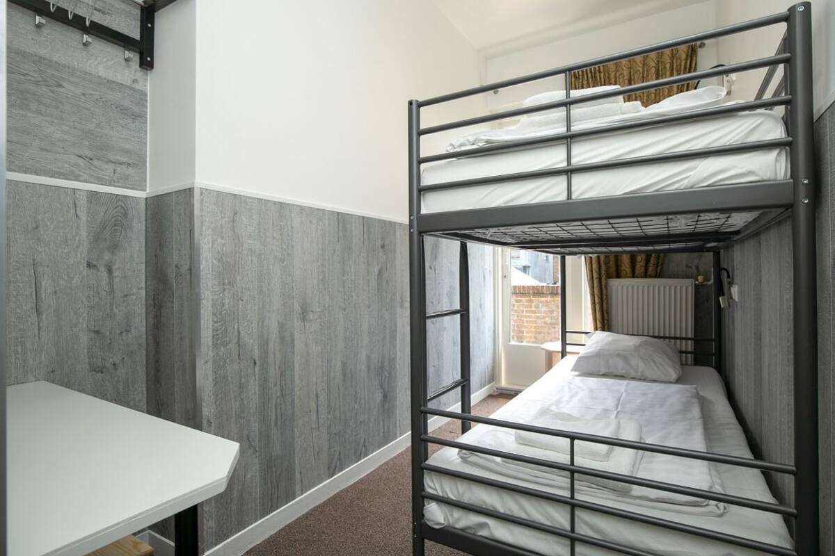 A bunk bed room with a white desk and a window with curtains.