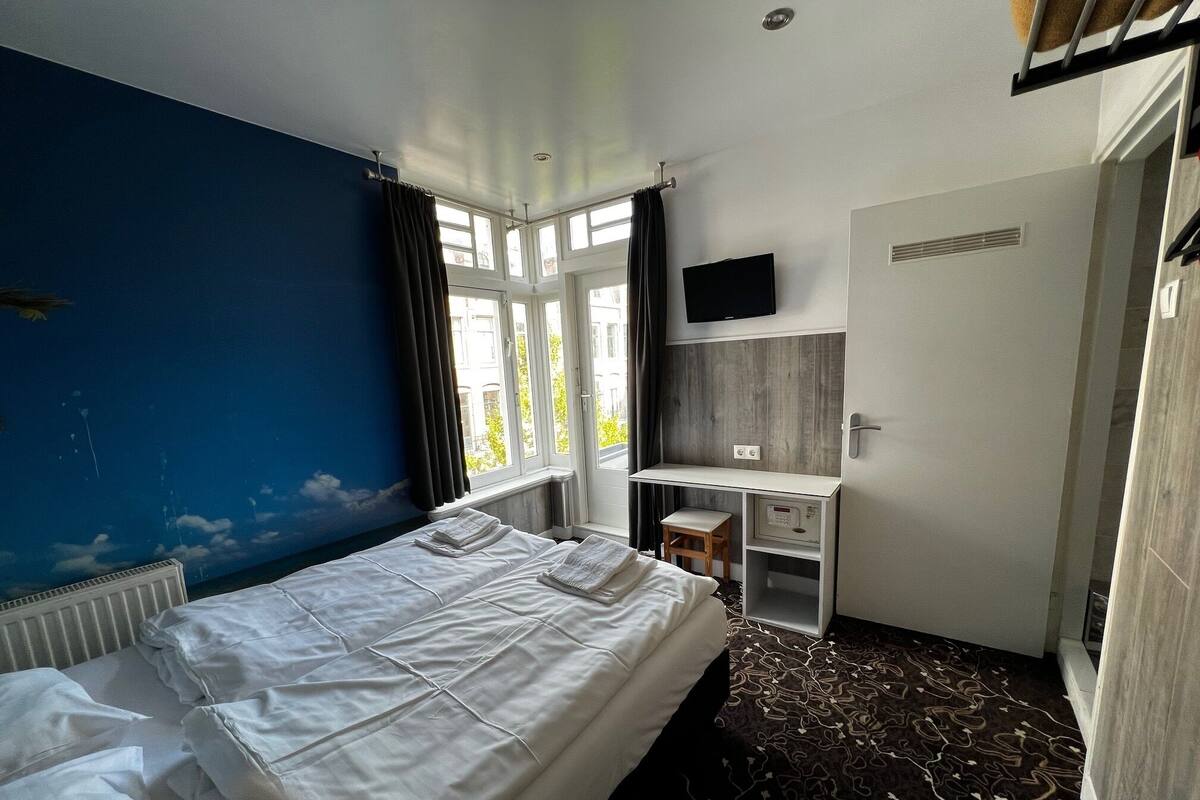 A hotel room with a bed, a desk, a TV, and a window with curtains.