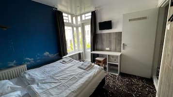 A hotel room with a bed, a desk, a TV, and a window with curtains.