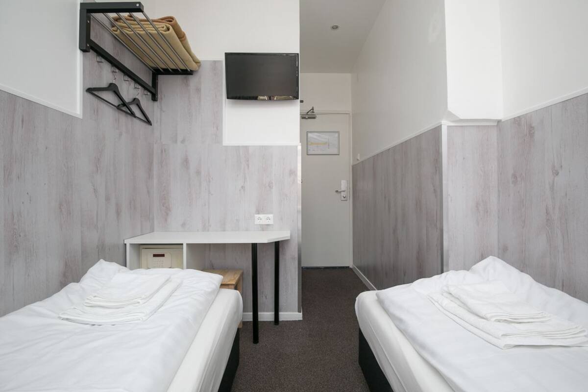 A hotel room with two beds, a desk, a TV, and a shower area.
