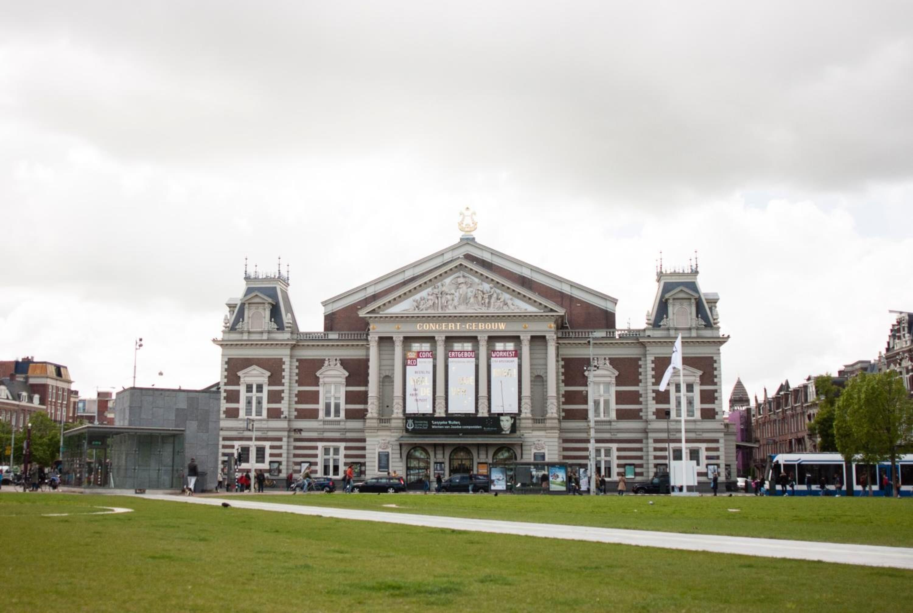 A large, historic building with a central entrance and two symmetrical towers, surrounded by a grassy area and other buildings.