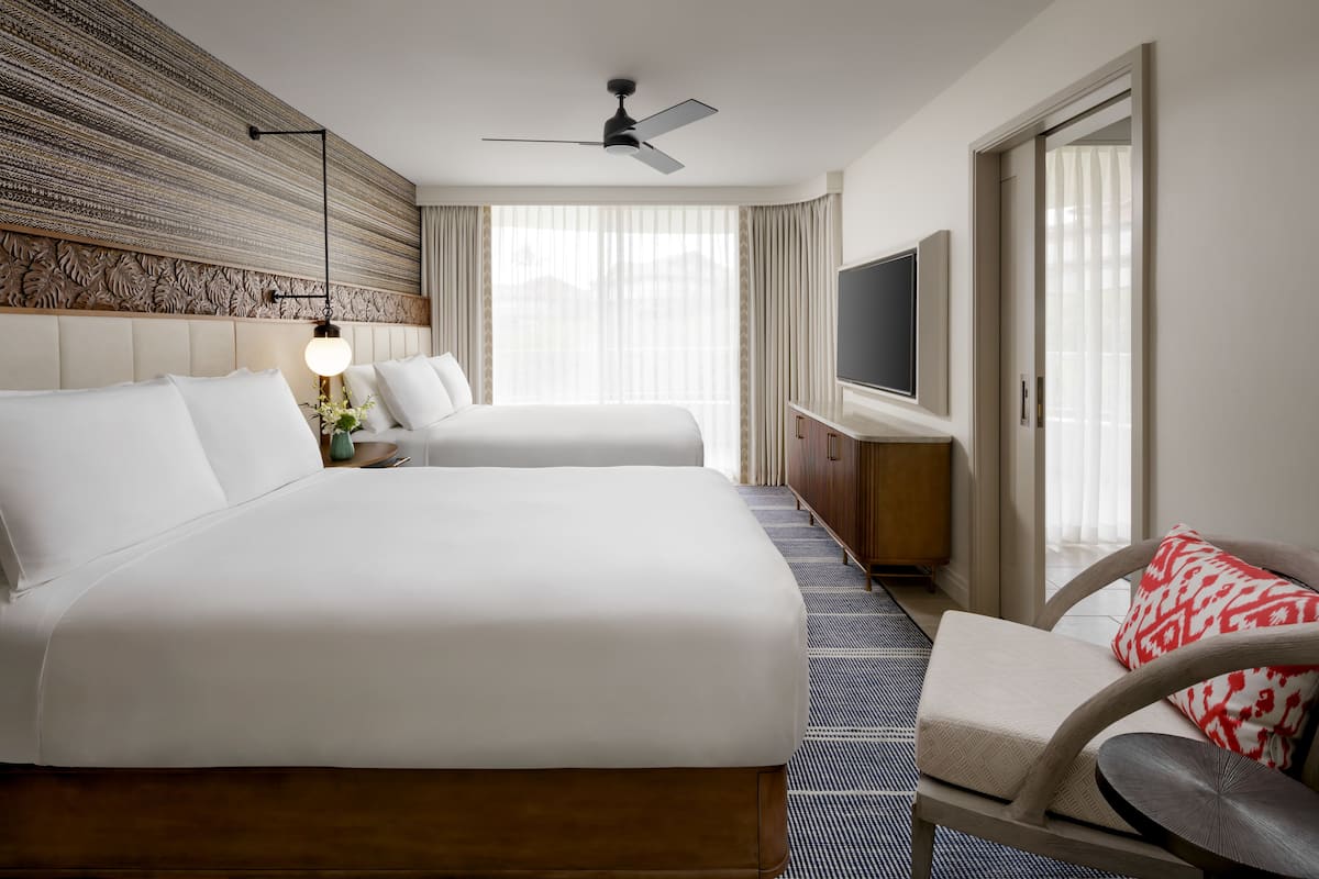 A hotel room with two beds, a TV, a ceiling fan, and a large window with curtains.