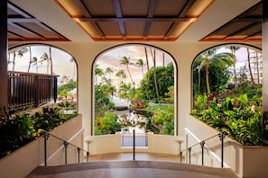 A staircase with a view of a garden, palm trees, and a bridge.