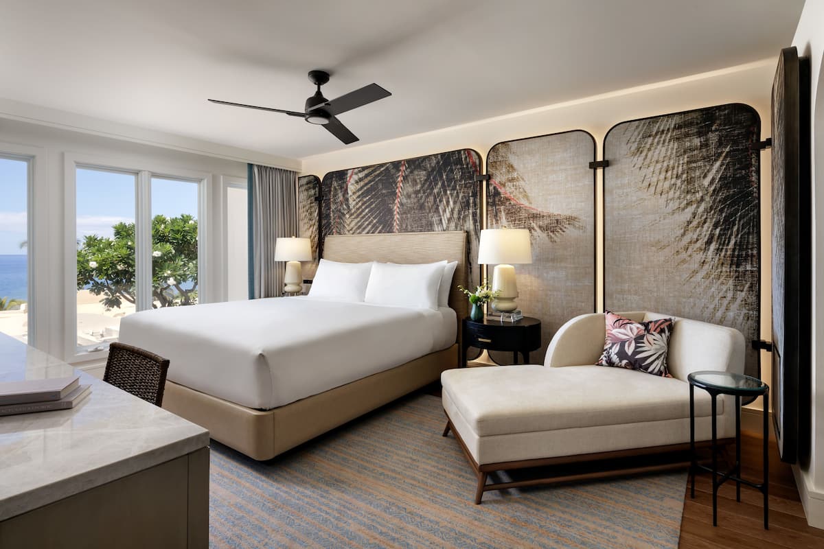 A hotel room with a large bed, a sofa, a desk, and a view of the ocean.