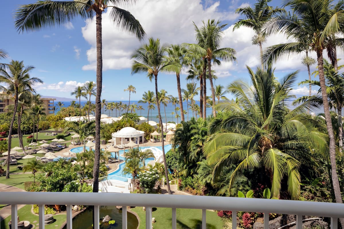 A resort with a pool, palm trees, and a view of the ocean.