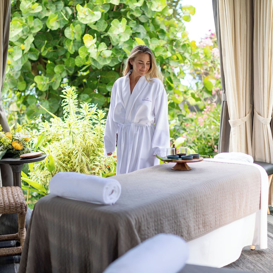 A spa room with a massage table, a small table with a flower arrangement, and a wicker chair.