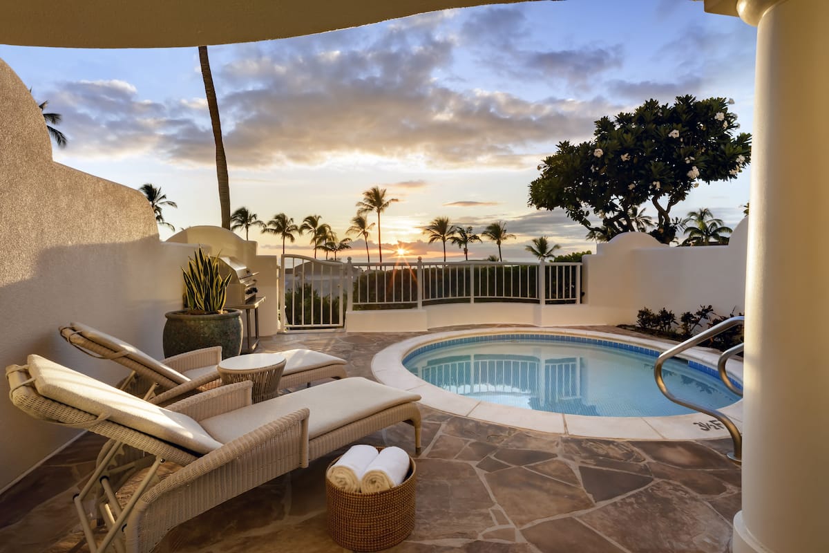 A poolside area with lounge chairs, a small pool, and a view of palm trees and sunset.