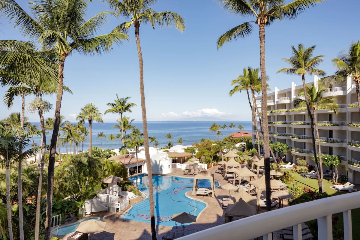 A resort with a pool, palm trees, and a view of the ocean.