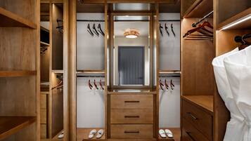 Un vestidor con estantes de madera, puerta con espejo y espacio para colgar zapatos y cinturones.