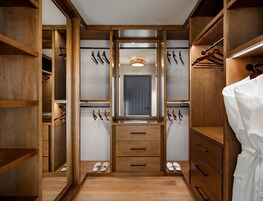 Un vestidor con estantes de madera, puerta con espejo y espacio para colgar zapatos y cinturones.