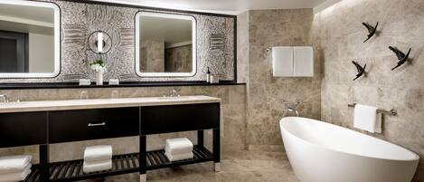 A modern bathroom with a freestanding bathtub, a large mirror with a leaf pattern, and a black vanity with multiple towel holders.