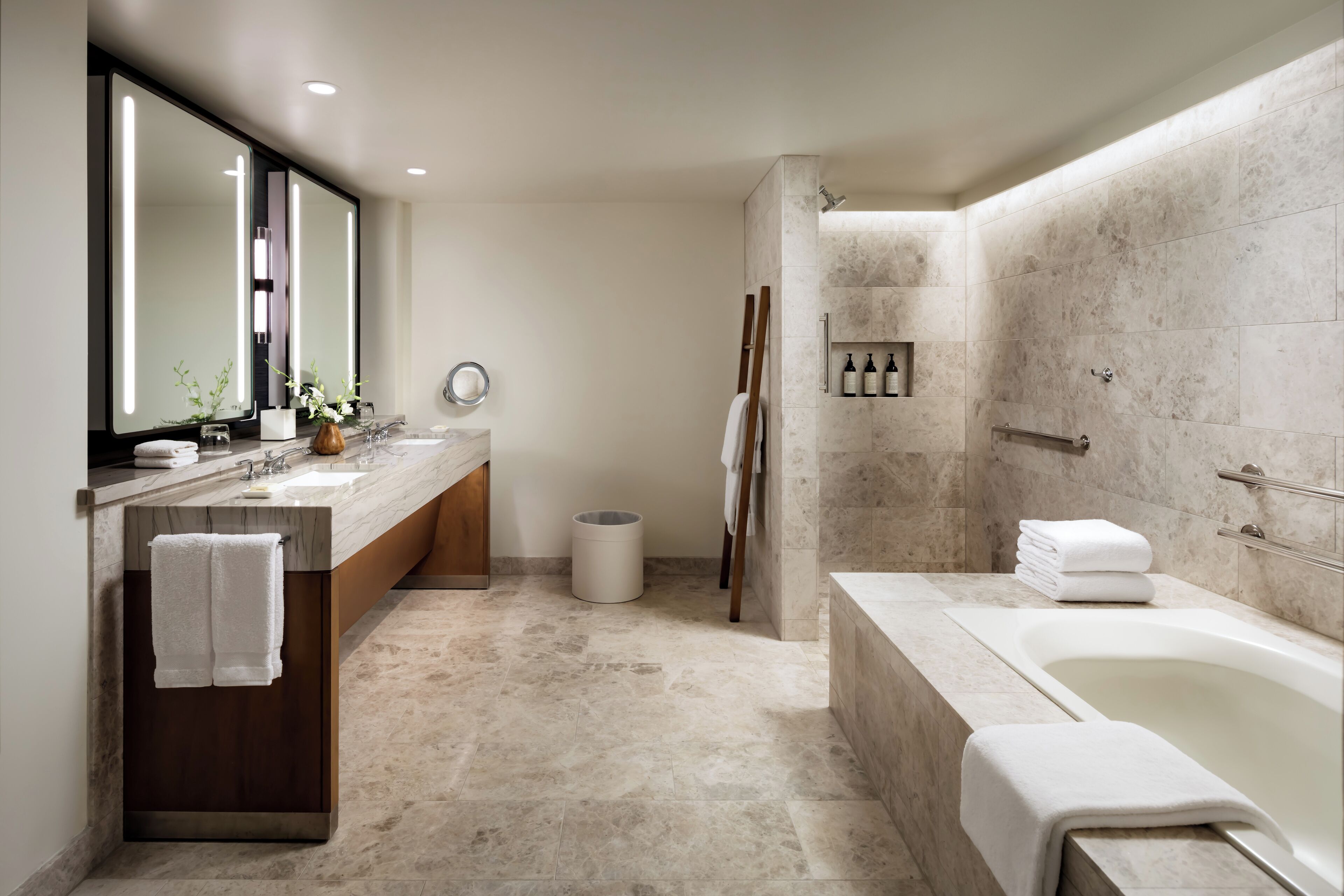 A modern bathroom with a large mirror, two sinks, a bathtub, and a shower area.